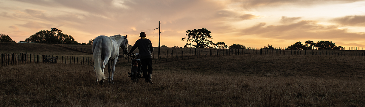 JUNIPER_JR-7220_SAM_Backshot_walking his motorbike and horse across the field